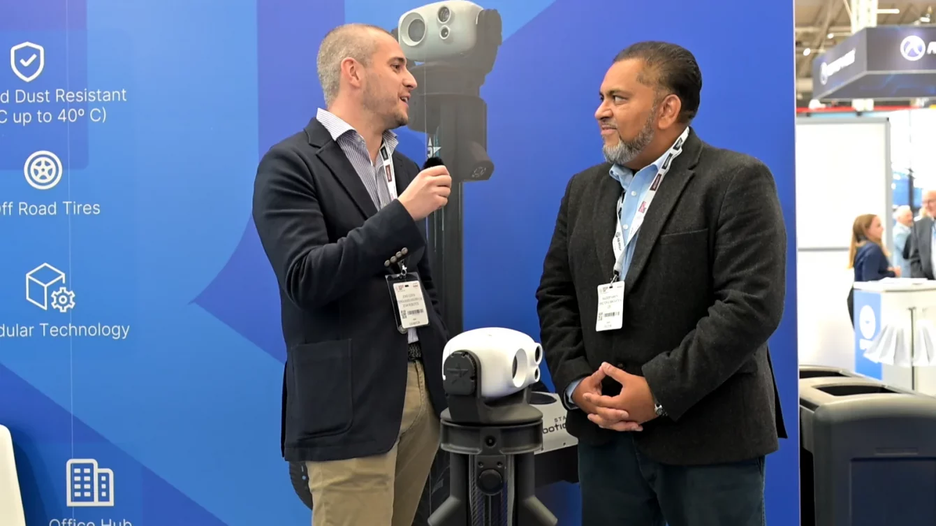 Dos responsables de Star Robotics y CIS Security conversan junto al robot Watchbot en un stand de feria de seguridad
