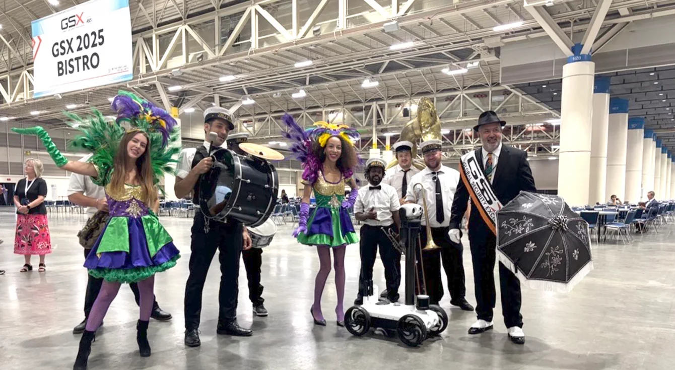 Robot Watchbot junto a músicos con trajes de Mardi Gras en el pabellón de la feria GSX 2025 de Nueva Orleans