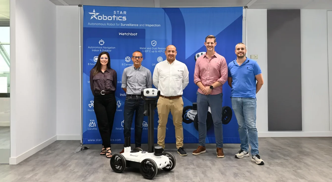 Cinco integrantes de los equipos de Star Robotics y Wilson James posando con el robot Watchbot ante un panel de la marca